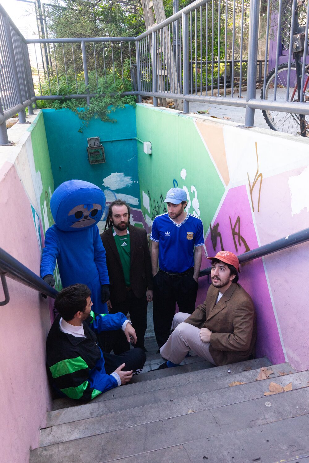 Los cinco de Los Maratonistas en la bajada de una escalera pintada de colores, con el perezoso celeste entre ellos.