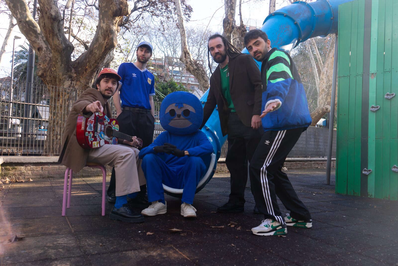 Los cinco de Los Maratonistas en una plaza, alrededor del tobogán azul, con el perezoso sentado en el medio.